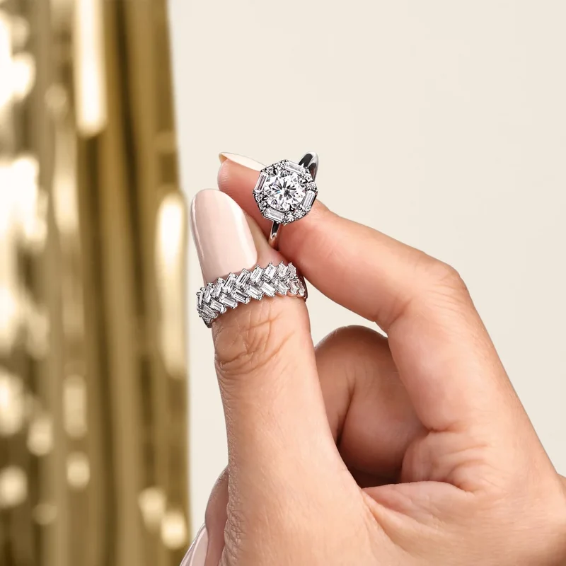 Two Gabriel & Co. diamond rings held between a thumb and finger